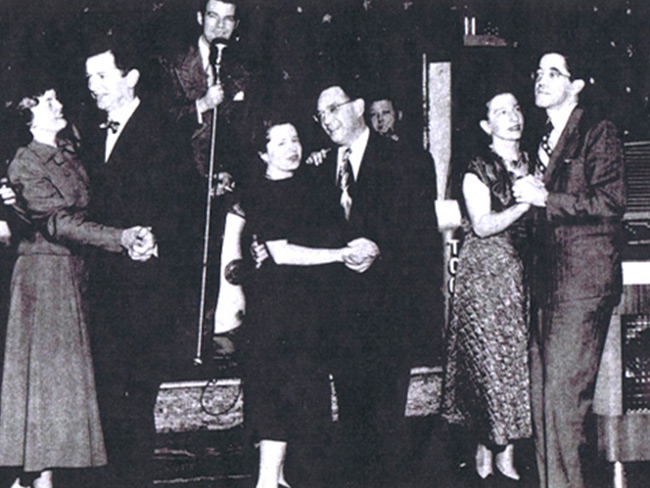 Black  and white photo of three couples partner dancing dressed in 1940s attire
