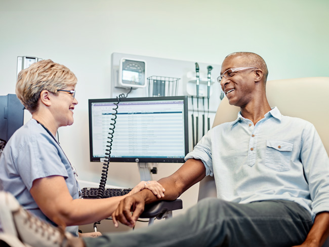 man seated in exam room with medical care worker