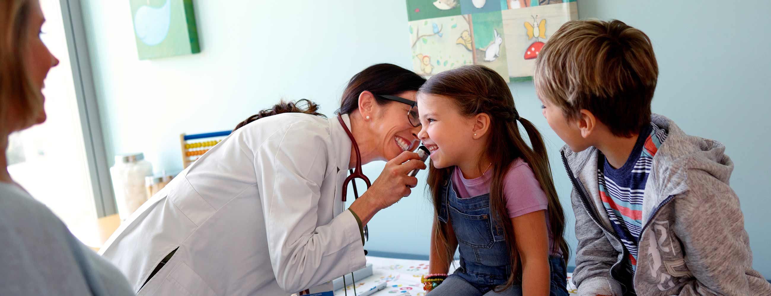 A smiling physician examining a young girl's ear with an otoscope.